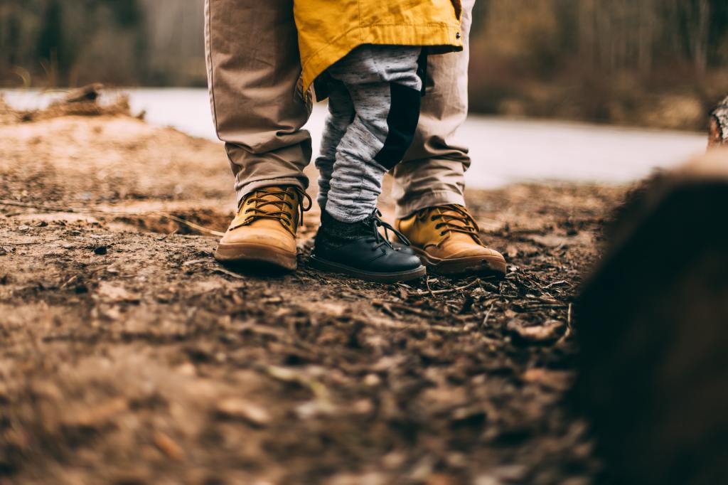 Father and son's legs pictured standing together on a dirt path, each in boots